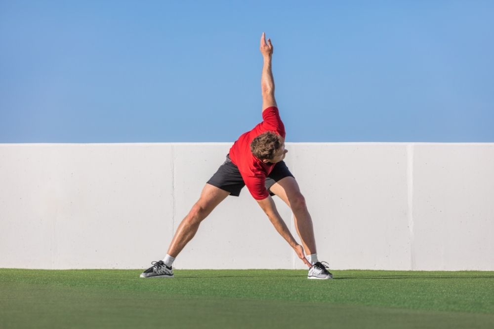 Man doing alternating toe touches outside in the grass